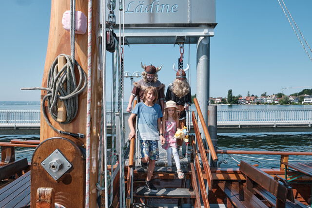 Zwei Wikinger, ein Junge und ein Mädchen gehen an Bord der Lädine.